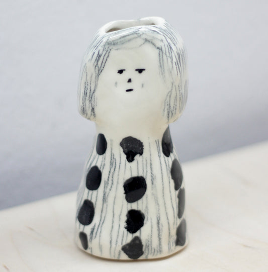 Ceramic vase shaped like a person with black polka dots on a white surface